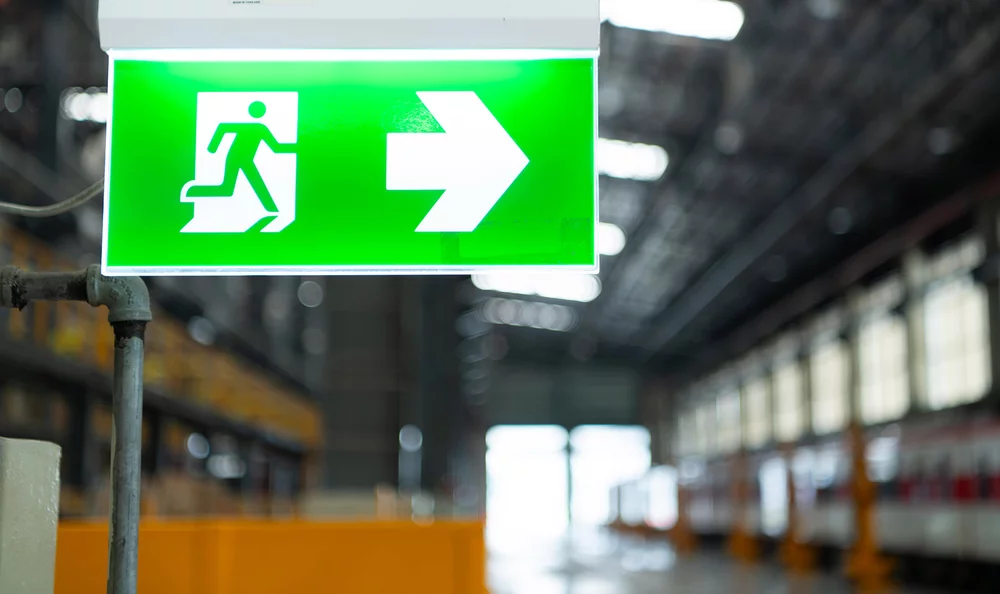 Bild mit beleuchtetem Rettungsweg-Zeichen. Auch Lage u. Anzahl der Rettungswege werden in Teil B beschrieben.